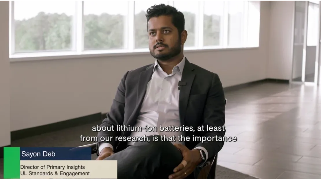 A man wearing a dark suit sits in a modern, bright office space. The caption reads, "about lithium-ion batteries, at least from our research, is that the importance." A name label reads "Sayon Deb, Director of Primary Insights, UL Standards & Engagement.